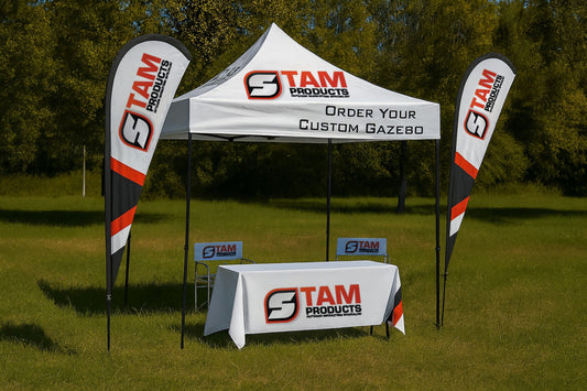 Stam Products branded white gazebo combo with flags, chairs, and tablecloth set up outdoors on grass.