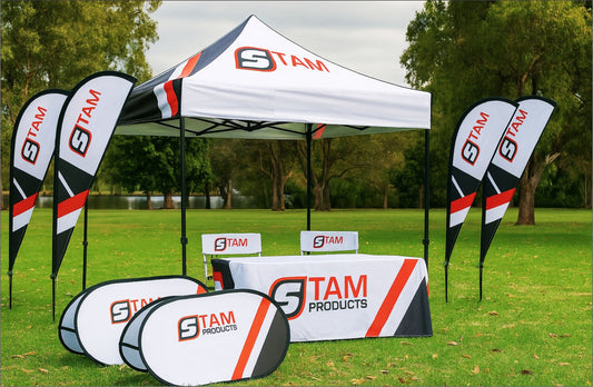 Stam Products custom branded gazebo combo with printed canopy, flags, pop-up banners, table cloth, and directors chairs set up on green grass outdoors