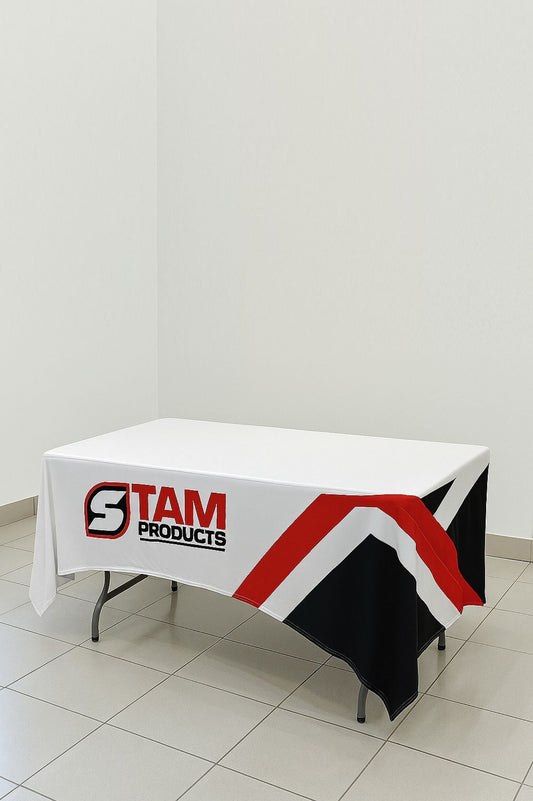 Custom printed branded table cloth by Stam Products with logo and red, white, black design on a folding table in a plain room.
