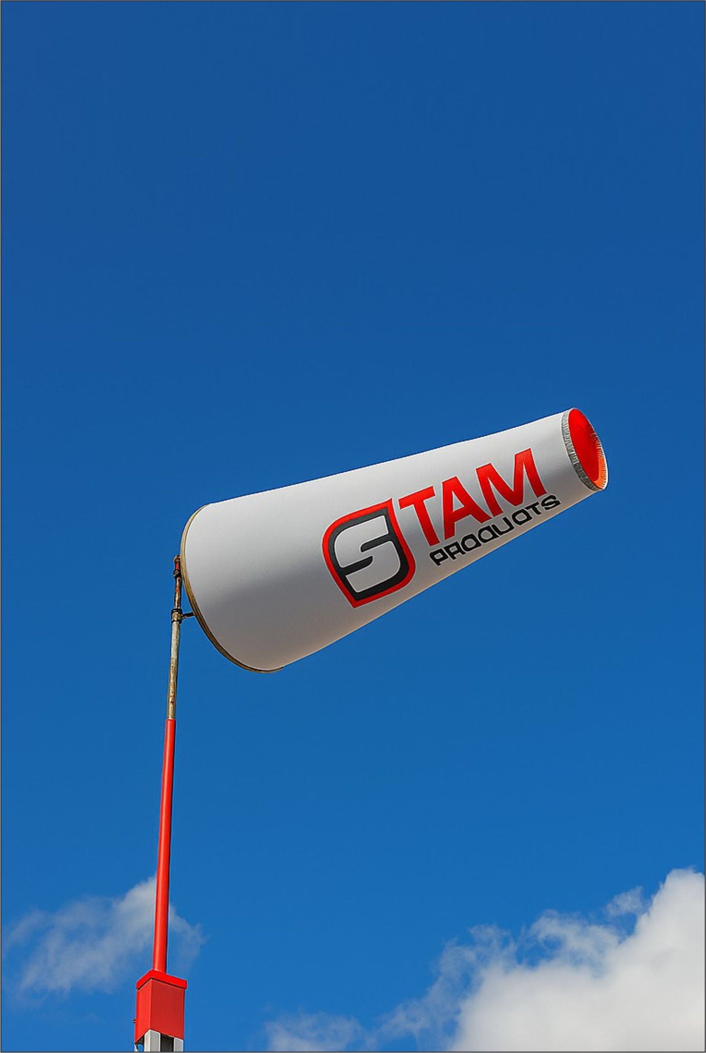 Custom branded white and red Stam Products wind sock banner on a pole against a clear blue sky